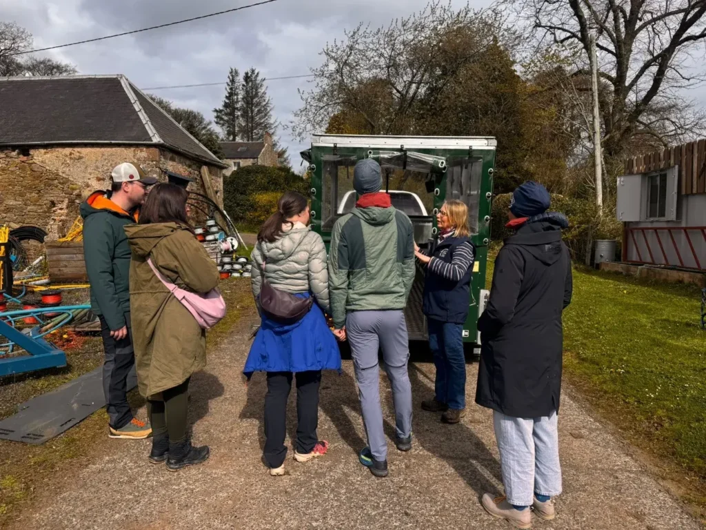 Lucy talking to a small tour group beside the farm trailer at Bairnkine